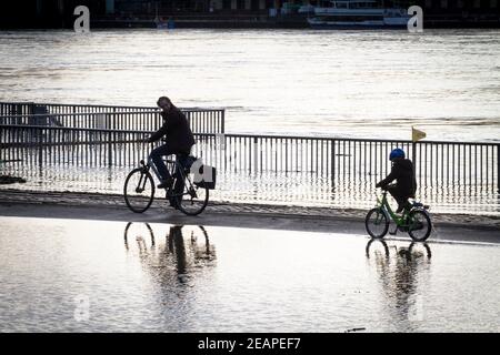 Inondation du Rhin le 4 février 2021, enfant et adulte à vélo à travers l'eau sur la rive inondée du Rhin à Deutz, Cologne, allemand Banque D'Images