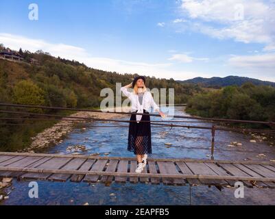 Belle femme en chapeau et robe promenade sur le pont en bois de l'autre côté de la rivière de montagne. Vue aérienne du dessus, concept de voyage Banque D'Images