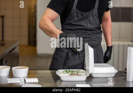 Chef préparant un plat à une boîte dans un restaurant pour le service de livraison de nourriture à la maison, commande en ligne Banque D'Images