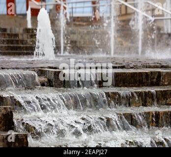 De denses ruisseaux d'eau débordent sur le bord de la fontaine en pierre. Banque D'Images