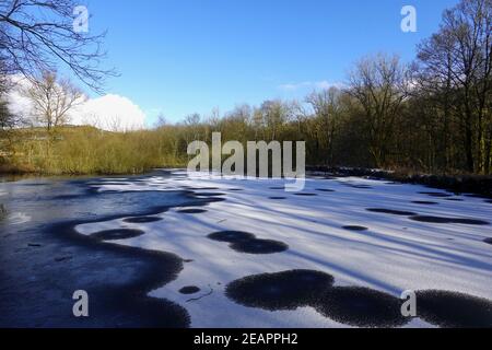 La neige couvre une grande partie de l'étang de la réserve naturelle de New Mills, dans le Derbyshire Banque D'Images