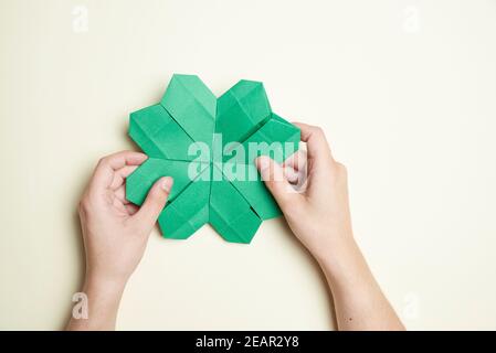 Trèfle à quatre feuilles en papier, origami, tenu par deux mains de jeune femme sur un fond clair. Concepts de chance et de la Saint-Patrick. Image avec co Banque D'Images