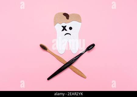 Une dent coupée en feutre, affectée par des caries, avec des brosses à dents croisées, sous forme de crâne et d'os. Pose à plat. Fond rose. Le concept de de Banque D'Images