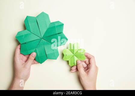 Paire de shamrocks à quatre feuilles d'origami, en papier vert, tenu par deux mains de jeune femme sur un fond clair. Concepts de chance et St. Patrick's D. Banque D'Images