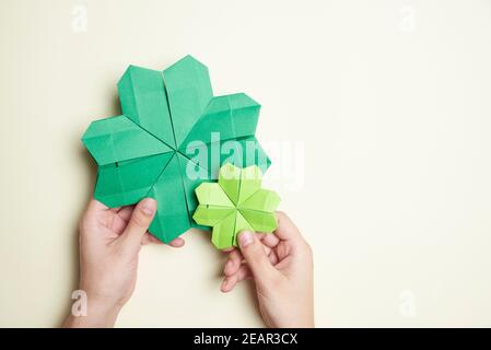 Paire de trèfle à quatre feuilles d'origami, en papier vert, tenu par deux mains de jeune femme sur un fond clair. Concepts de chance et de la Saint-Patrick Banque D'Images