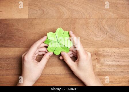 Les mains d'une jeune femme tiennent et le trèfle d'origami fait de papier vert clair sur un fond en bois. Concepts de chance et de la Saint-Patrick. Image avec Banque D'Images