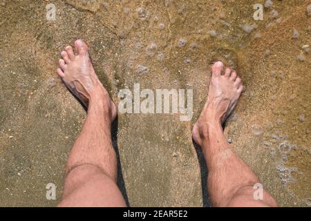 Les jambes des hommes sur le sable de la mer près de mer vague Banque D'Images