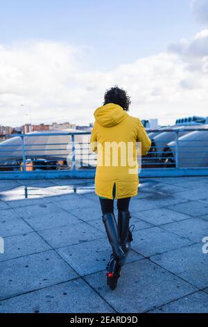 Une jeune femme en manteau jaune prépare et utilise son skateboard électrique. Banque D'Images