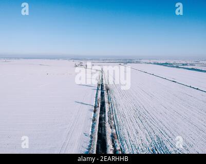 Photographie aérienne d'une route entre les champs couverts de neige sous le ciel bleu clair Banque D'Images