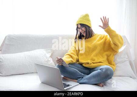 Élégante belle fille brune en lunettes et un chapeau assis sur le canapé devant un ordinateur portable et communique en ligne espace de copie. Banque D'Images