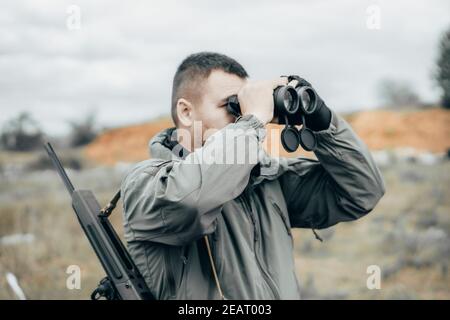 Homme avec une carabine regardant travers des jumelles