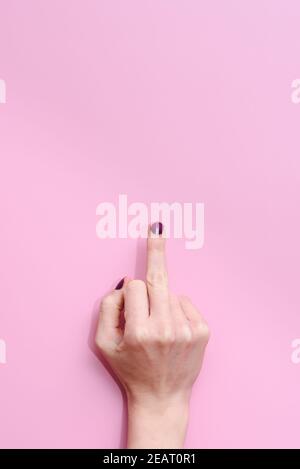 studio vertical prise de la main d'une femme caucasienne élevant le viseur moyen montrant un geste offensant sur un fond rose. Concept de disco pour femmes Banque D'Images
