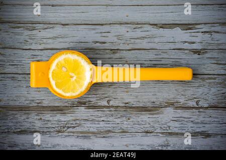 Un demi-citron dans un presse-fruits jaune sur fond de bois bleu clair. Banque D'Images