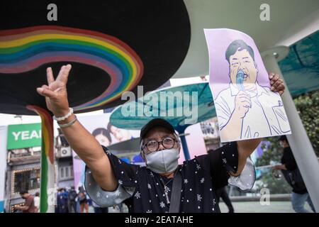 Une personne âgée salue les trois doigts tout en tenant le portrait de l'activiste Parit 'Penguin' Chiwarak lors d'une manifestation "make noise" pour dénoncer le récent coup d'État militaire de la junte au Myanmar et rejeter l'article 112 du code pénal thaïlandais.des milliers de manifestants pro-démocratie ont organisé une manifestation, A l'extérieur du centre commercial MBK de Siam, appelé « Make Noise » en faisant des coups d'ustensiles de cuisine en solidarité avec les manifestants anti coup d'État militaire au Myanmar et en rejetant la section 112 du code pénal thaïlandais. Les manifestants exigent également la démission du Premier ministre thaïlandais, Prayut Chan-o-cha and Banque D'Images