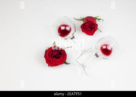 Roses rouges et verres à vin avec vin rouge sur fond blanc. Vacances et le jour de Valentin romantique appartement, concept de dessus de vue. Banque D'Images