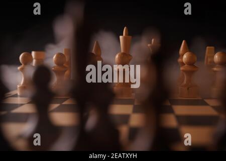 Gros plan de pièces d'échecs blanches à bord avec de la vapeur dissipant. Deux rangées de figures en bois sur échiquier sur fond noir. Concept d'intelligence, Banque D'Images