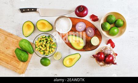 Moitiés d'avocat, morceaux, limes et oignons, tasse avec sel - ingrédients de base de guacamole et couteau de chef sur table de travail blanche, plan de travail plat photo Banque D'Images