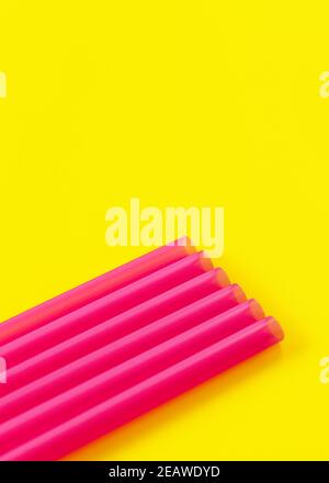 Six pailles à boire en plastique rose sur le carton jaune, formant une ligne diagonale - détail résumé gros plan, espace pour le texte ci-dessus Banque D'Images