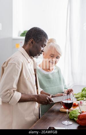 Homme afro-américain préparant une salade près d'une femme senior dans la cuisine Banque D'Images