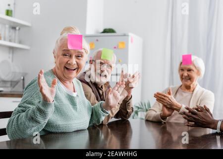 des amis âgés enthousiastes et multiculturels avec des notes collantes sur les fronts jeu deviner qui joue dans la cuisine Banque D'Images