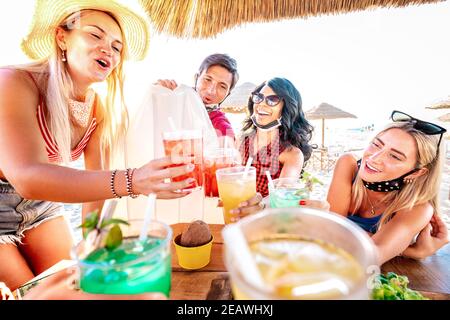 Des amis heureux buvant au bar à cocktails de la plage portant un masque facial - Nouveau concept d'été normal avec les gens qui s'amusent ensemble toaster les boissons Banque D'Images