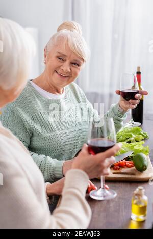 bonne femme senior tenant un verre de vin rouge et regardant à un ami retiré sur un premier plan flou Banque D'Images