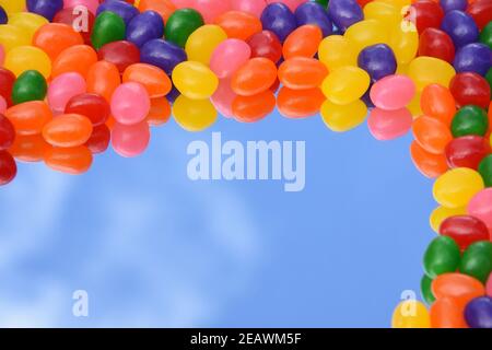 Jelly beans colorés sur le miroir avec le reflet du ciel bleu avec fond blanc de nuage. Vue de dessus. Copier l'espace. 3 dimensions. Banque D'Images