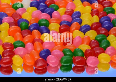 Jelly beans colorés sur le miroir avec son reflet contre le ciel bleu. Pour une utilisation en arrière-plan. Vue de dessus. 3 dimensions. Banque D'Images