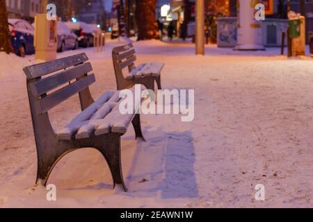 Paysage de nuit et concentration sélective sur le banc de rue extérieur recouvert d'une épaisse couche de neige sans personnes sur le trottoir en Allemagne. Banque D'Images