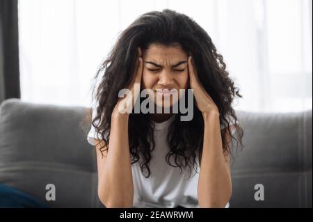 Souriante multiraciale noire curly fille utilise le téléphone cellulaire, parler avec des amis ou la famille tout en étant assis sur le canapé dans le salon et regarde l'appareil photo, commu Banque D'Images