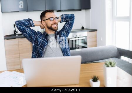 Un pigiste positif se détendant sur le lieu de travail et souriant. Homme d'affaires caucasien confiant, assis au bureau à domicile, en pause loin Banque D'Images