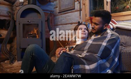 Jours d'hiver paresseux. Jeune couple appréciant les vacances d'hiver. Embrassant couvert de couverture et parlant près de la cheminée. Photo de haute qualité Banque D'Images