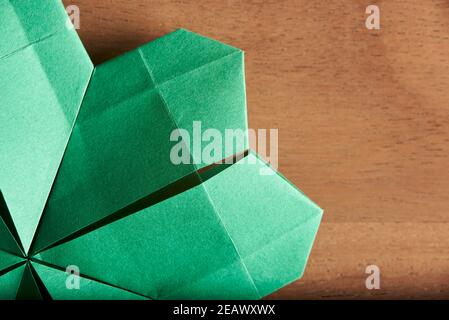 Détail d'un trèfle à quatre feuilles en papier vert plié suivant la technique de l'origami, sur fond de bois. Flat lay, gros plan. Banque D'Images