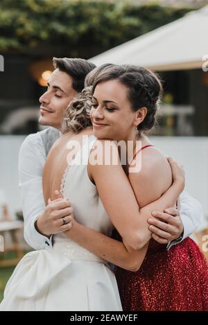 Soeur de la mariée embrassant un jeune couple sur leur jour de mariage Banque D'Images