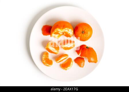 Epaillement de tangerines ou de clémentines dans une plaque blanche, isolée sur fond blanc Banque D'Images