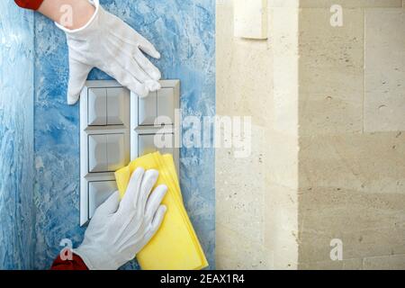 Désinfection des surfaces. Articles de maison en gants blancs nettoyer les interrupteurs d'éclairage avec un chiffon sur le mur à l'aide d'un vaporisateur d'alcool et d'un chiffon. Nouveau coronavirus normal Covid 19 c Banque D'Images