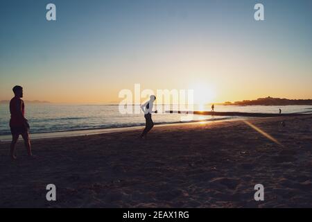 Jeunes jouant au rugby sur Gordons Bay Beach au coucher du soleil Banque D'Images