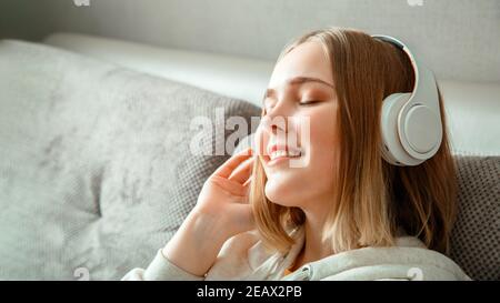 Bonne jeune femme assise sur un canapé dans un casque. Femme ou jeune fille se reposant, bonheur profiter d'écouter de la musique sur le canapé dans le salon. Portrait de la femme Banque D'Images