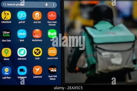 Sur cette photo, les logos Orderow, goPuff, Just Eat, Door Dash, Uber Eats, Wolt, McDelivery, Bolt, Glovo, Deliveroo, EASI, Jumia Food, Lidl plus, Deliveries, Lalamove et GRUB Hub sont affichés sur un écran de téléphone portable avec une image d'un courrier de livraison de nourriture affichée sur un écran d'ordinateur. Banque D'Images