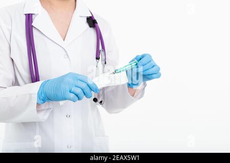 Une jeune infirmière dans un masque ouvre une seringue sur un fond blanc dans un manteau blanc, pour faire une vaccination, une injection. Le concept de vaccination et Banque D'Images