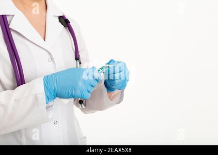 Une jeune infirmière dans un masque ouvre une seringue sur un fond blanc dans un manteau blanc, pour faire une vaccination, une injection. Le concept de vaccination et Banque D'Images