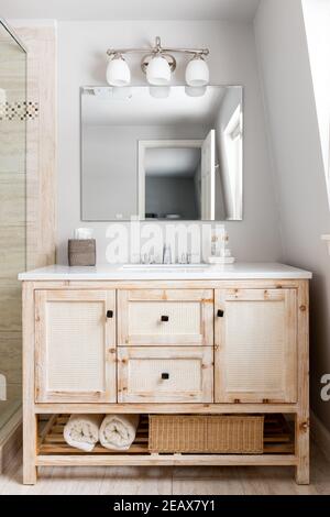 Une salle de bains luxueuse avec meuble-lavabo en bois, comptoir en granit blanc, robinet en chrome et lumière montée au-dessus du miroir. Banque D'Images