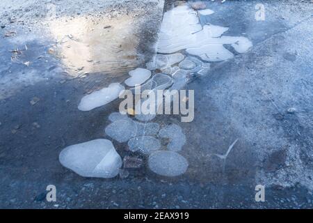 Sol gelé avec bulles d'air blanches dans l'eau. Gel glissant sur le trottoir de la ville. Banque D'Images