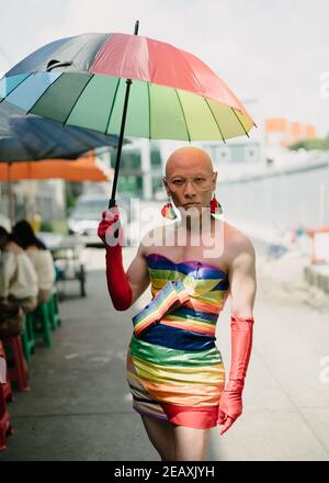 Portrait d'un queer asiatique vêtu d'une robe aux couleurs de l'arc-en-ciel, portant des gants rouges et tenant un parapluie aux couleurs de l'arc-en-ciel à Bangkok Thaïlande. Banque D'Images