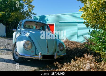 Avant sur Volkswagen Beetle bleu clair devant le garage assorti avec porte rouge contrastée. Banque D'Images