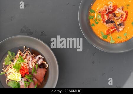 Soupe Tom Yam et soupe Ramen dans des bols sur fond gris arrière-plan Banque D'Images