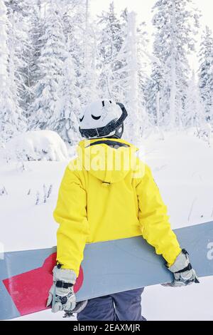 Femme snowboarder en costume brillant dans un casque de sport tient un snowboard. Sports extrêmes. Loisirs. Vue de l'arrière. Tir vertical Banque D'Images