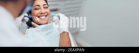 Bonne femme qui obtient un examen dentaire à la dentisterie. Dentiste utilisant de l'équipement dentaire pour l'examen des dents d'une patiente. Banque D'Images