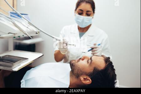 Dentiste examinant les dents d'un patient dans le fauteuil du dentiste à la clinique dentaire. Un patient de sexe masculin reçoit un traitement dentaire en clinique. Banque D'Images