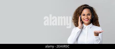 Service souriant femme afro-américaine sourit de porter des écouteurs le studio du centre d'appels a été tourné sur fond de bannière gris clair avec espace de copie Banque D'Images